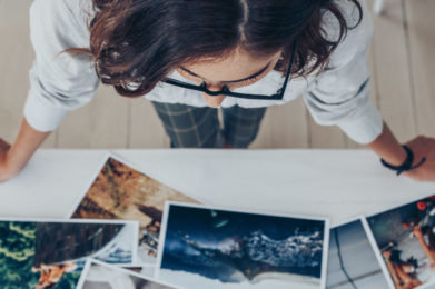 Top view of a female photographer working in studio looking at the prints lying on desk. Female photographer choosing the best image from several photo shoots.
